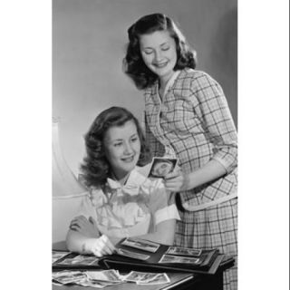 Two young women looking at pictures from photo album Poster Print (18 x 24)